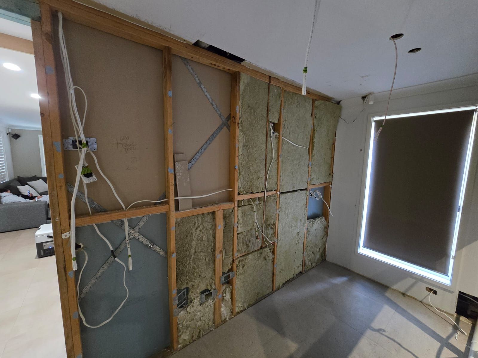 Interior view: Partially constructed wall with insulation and electrical wiring, adjacent to a window with a shade.