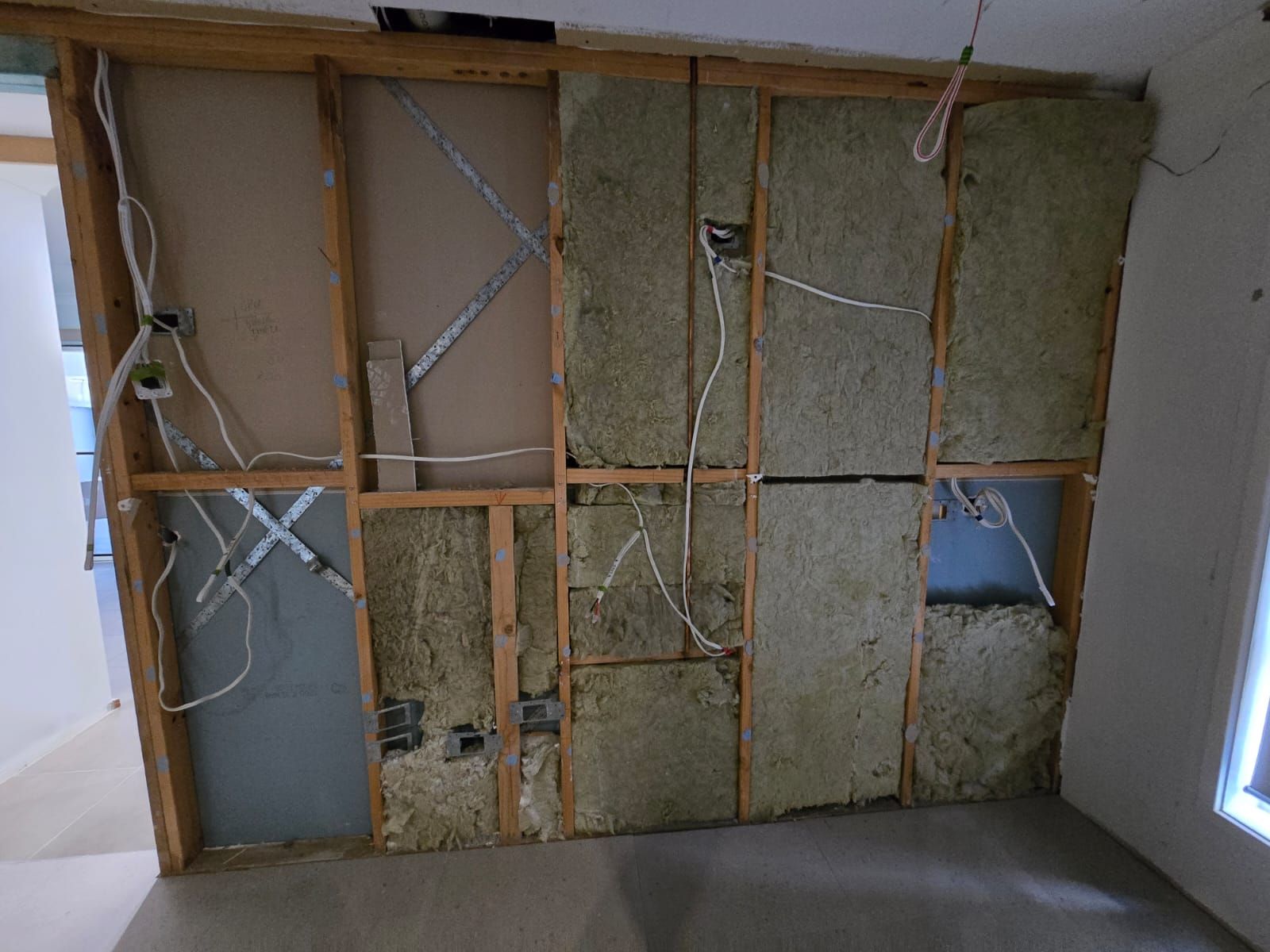 Interior wall framing with insulation, electrical wiring, and drywall, likely under construction.