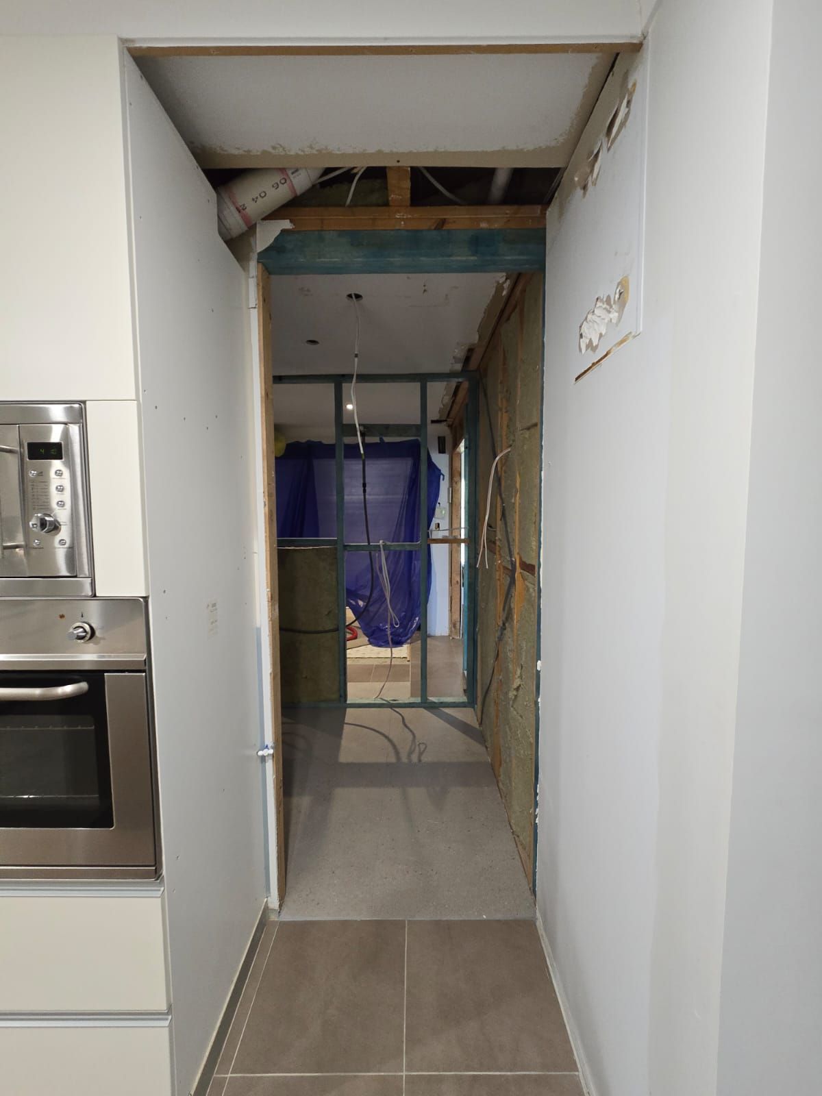 Hallway under renovation, showing exposed studs, insulation, and unfinished walls; door on left.