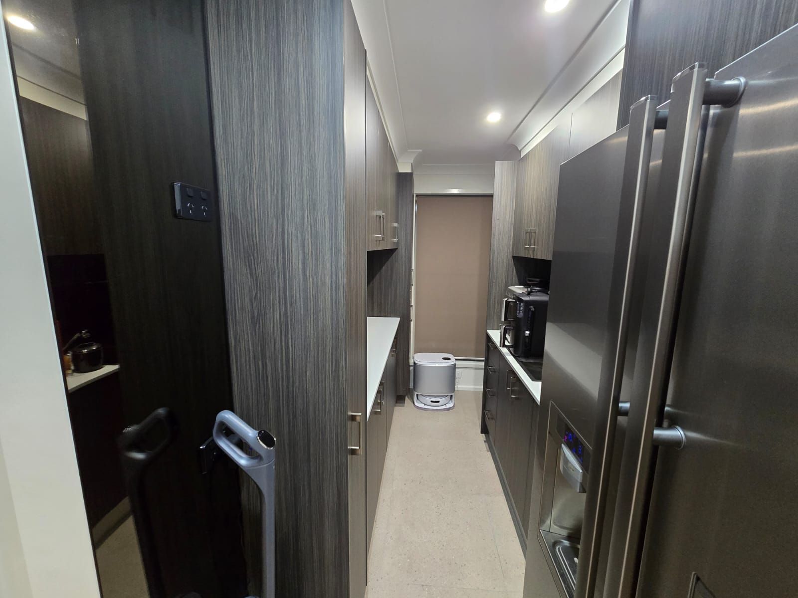 Narrow kitchen with dark wood cabinets, stainless steel appliances, and a vacuum cleaner.