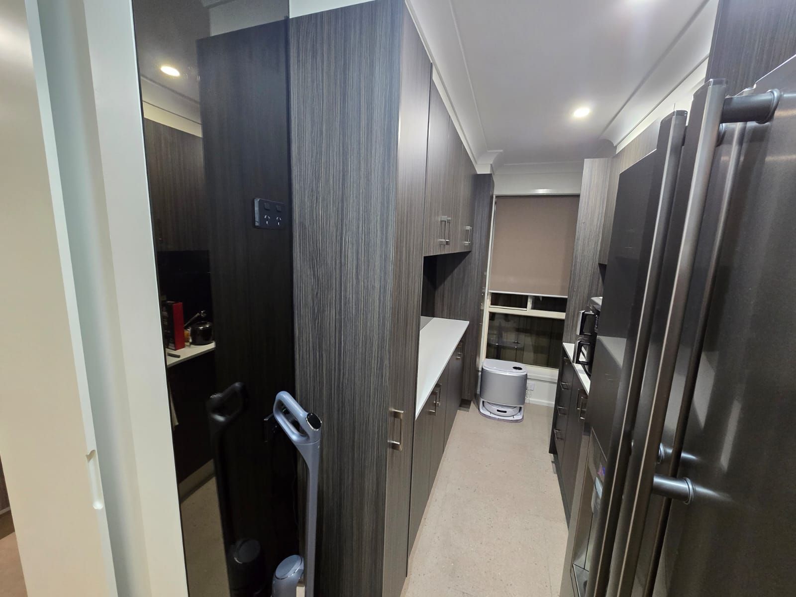 Narrow kitchen with dark wood cabinets and stainless steel refrigerator.