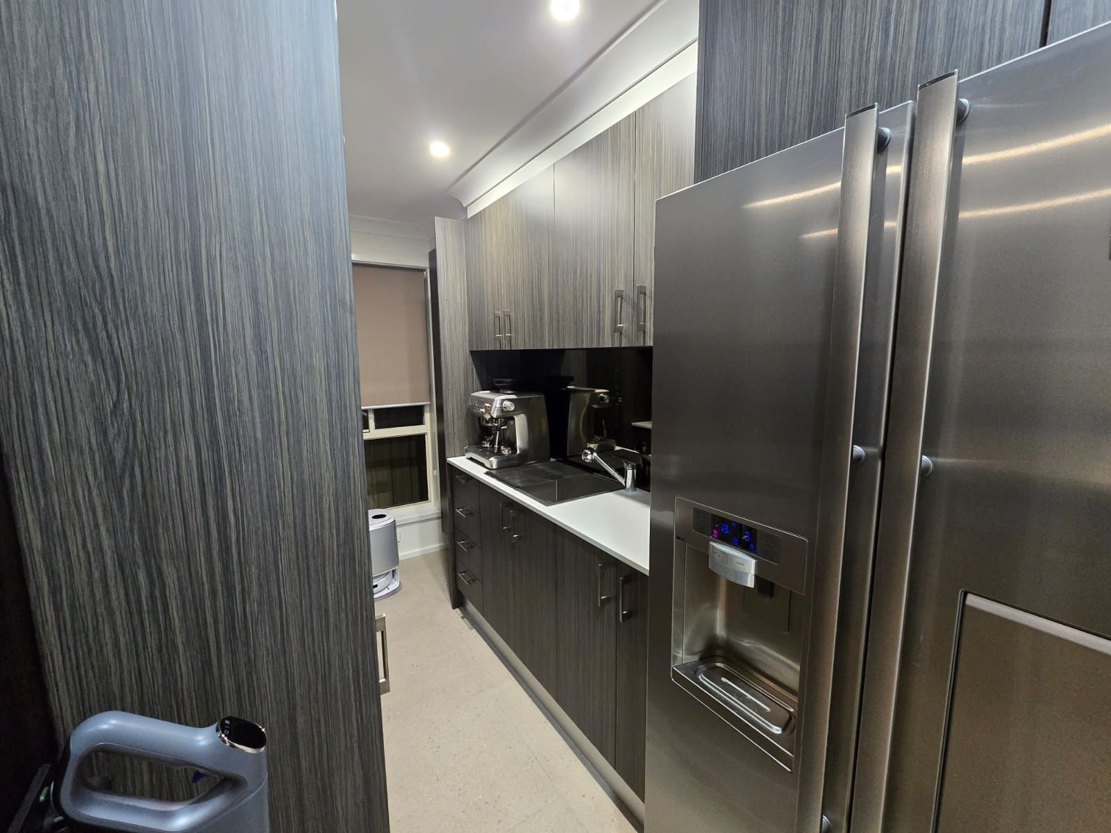 Narrow kitchen with gray cabinets, stainless steel refrigerator, and coffee machine.