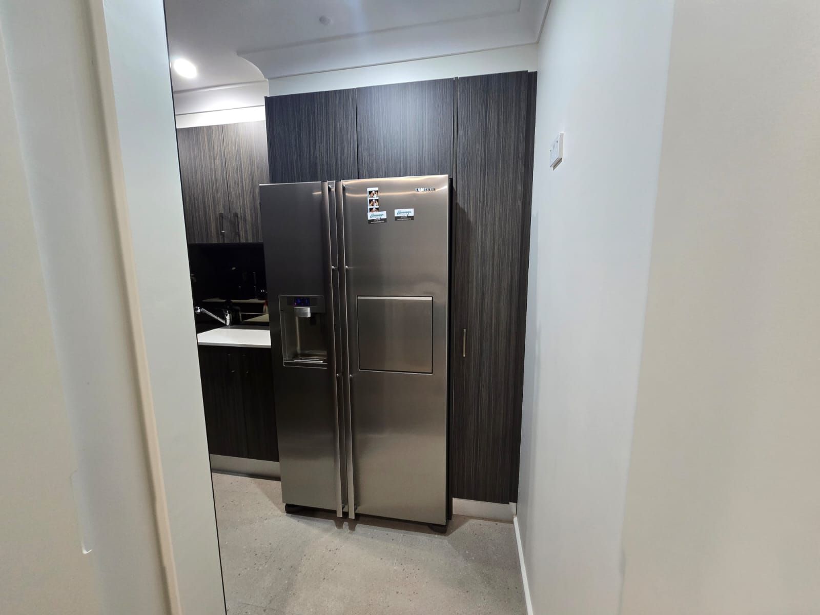Stainless steel refrigerator in a kitchen with dark wood cabinets, viewed from a doorway.
