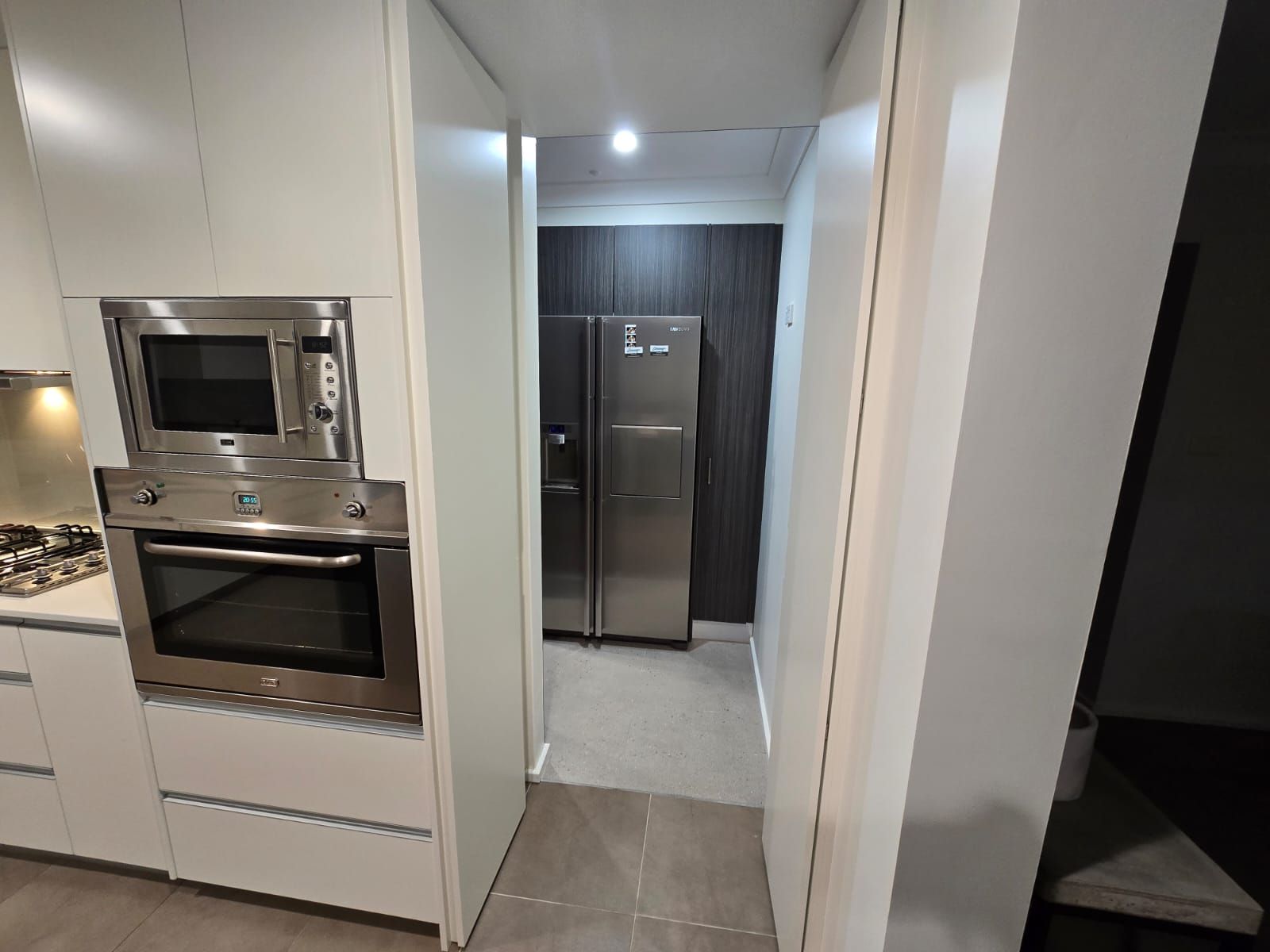 Kitchen with built-in oven and microwave, leading to a fridge in a separate space.