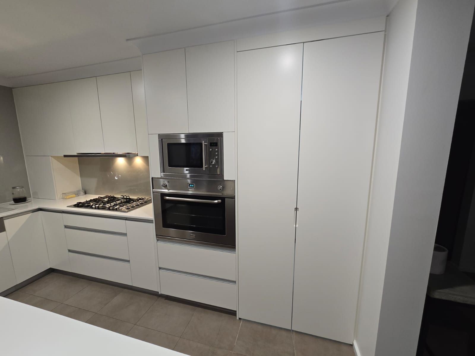White modern kitchen with built-in oven and microwave, cabinets and drawers.