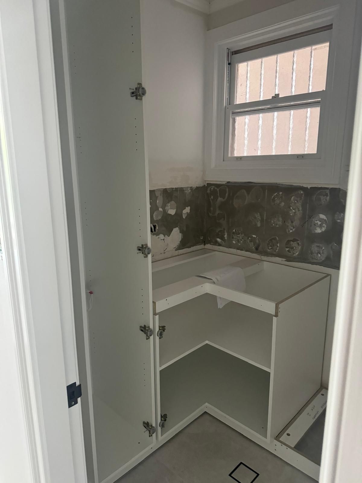 White cabinetry in a room with a window. The space is under construction, with exposed wall.