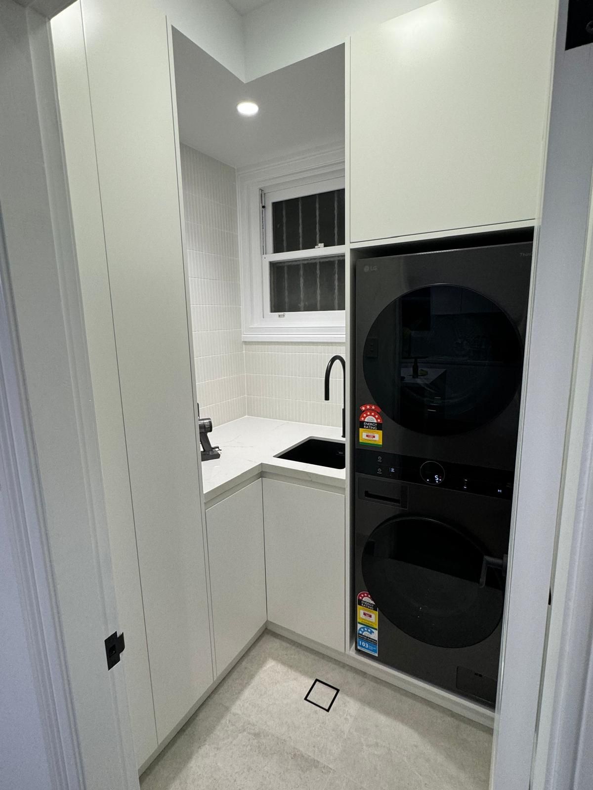 Small laundry room with white cabinets, a black sink and stacked black washer/dryer.