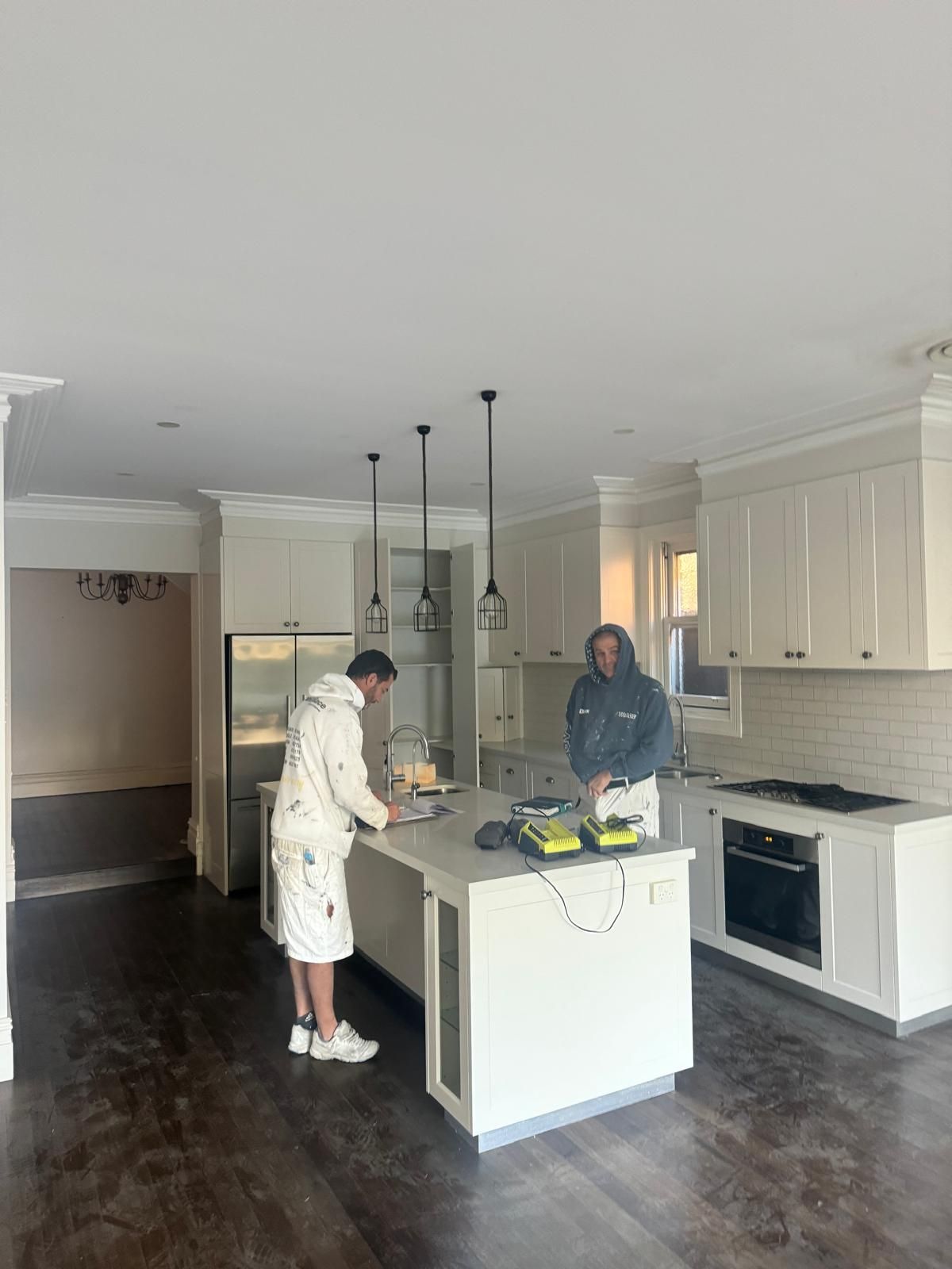 Two people working in a newly renovated white kitchen with island. One person stands at the island, and the other stands near the oven.