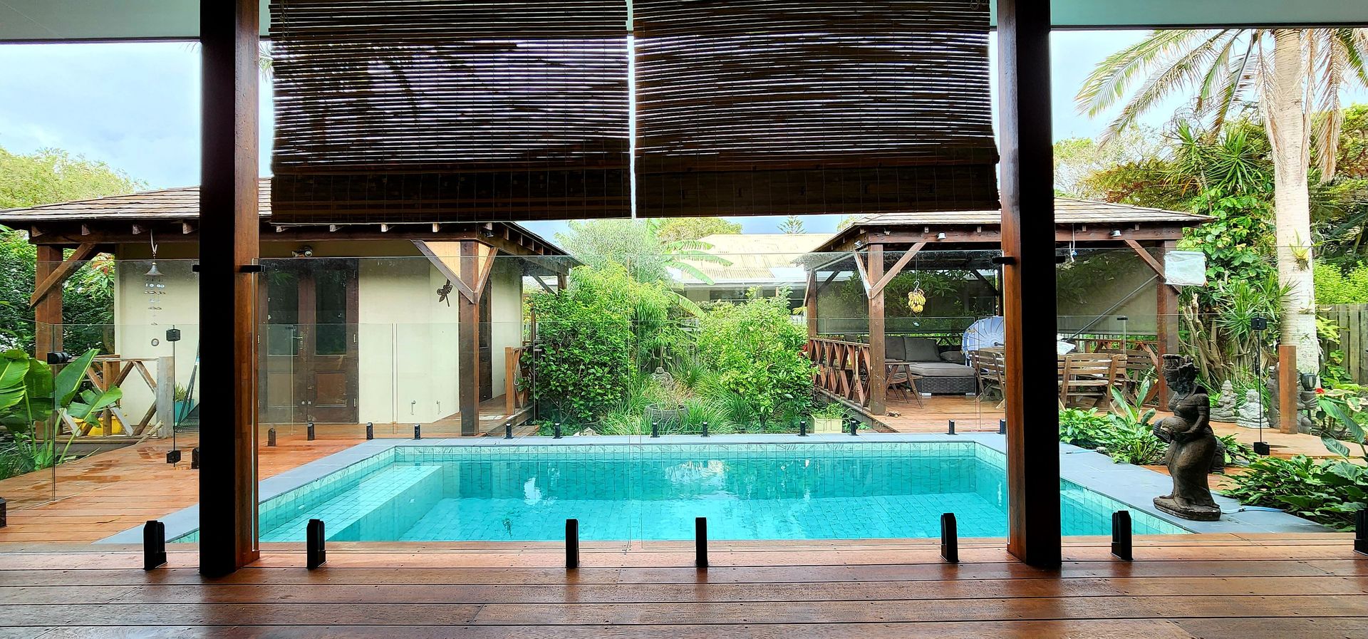 A backyard with a pool, surrounded by trees and a covered patio, it's a rainy day.