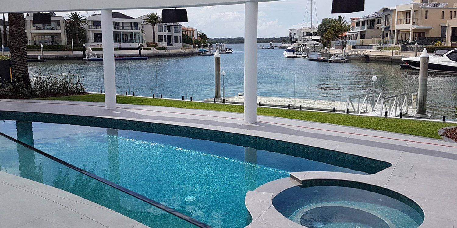 A pool overlooking a canal with houses and boats. The water is blue, the day is sunny.