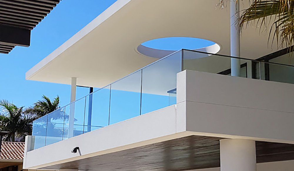 Modern white building with glass balcony railing against a bright blue sky.