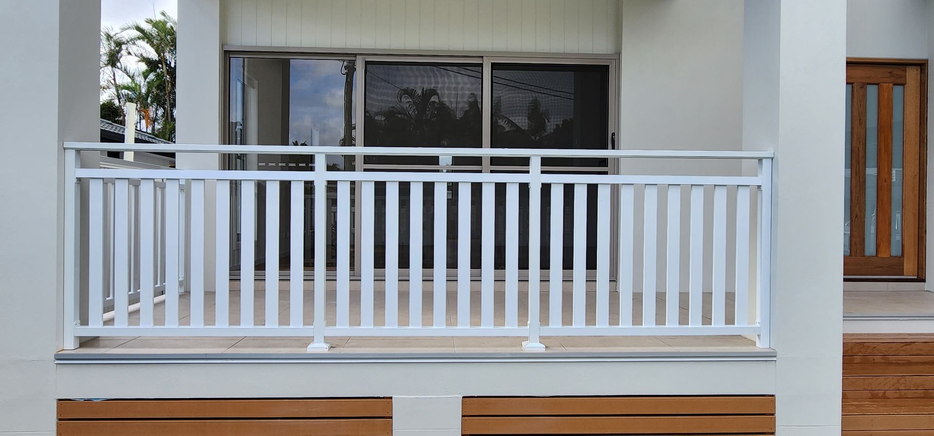 White balcony railing on a modern building. Brown bench in front. Wooden door on the right.