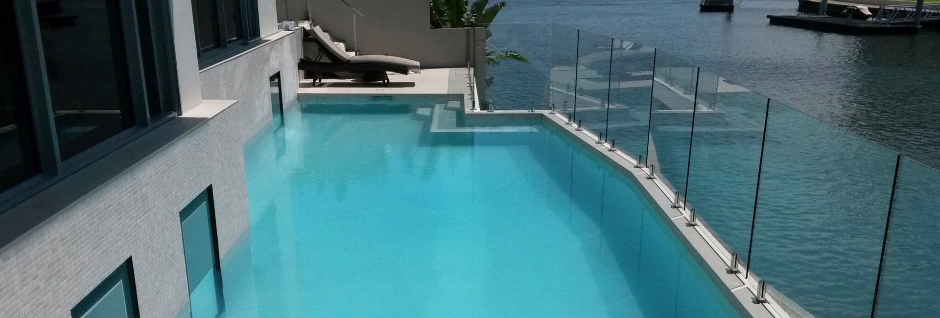 A luxurious outdoor swimming pool with a water view. The pool is blue and next to a building.