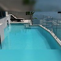 A rectangular pool with clear water, a lounge chair, and a waterfront view.