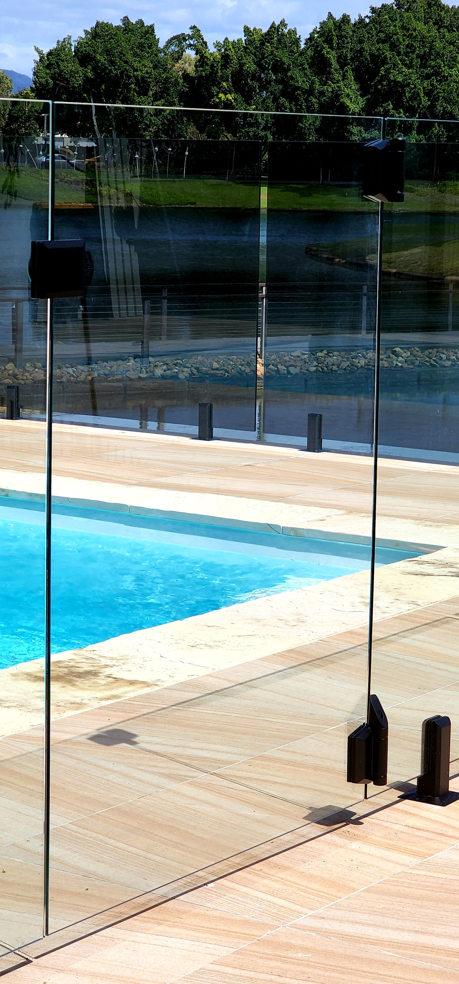 A clear glass fence surrounds a pool with blue water. The setting is outdoors.