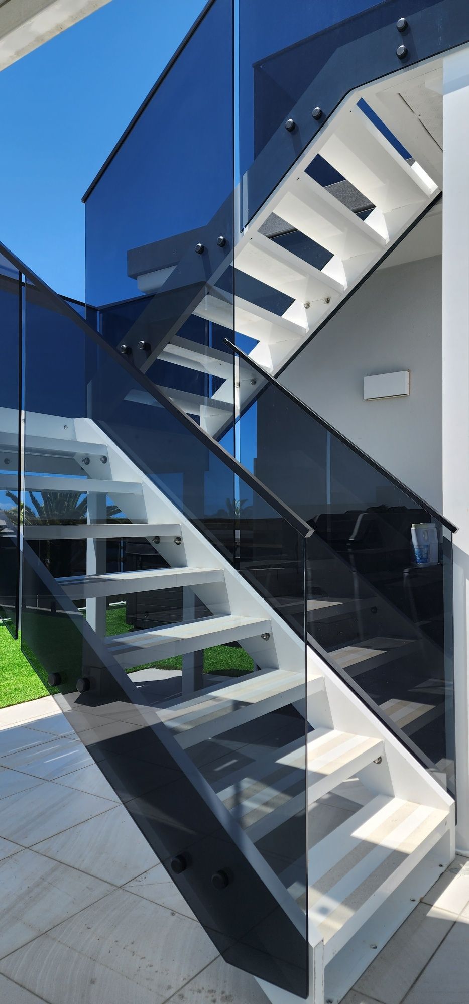 Modern staircase with glass railings, white steps, and blue sky.