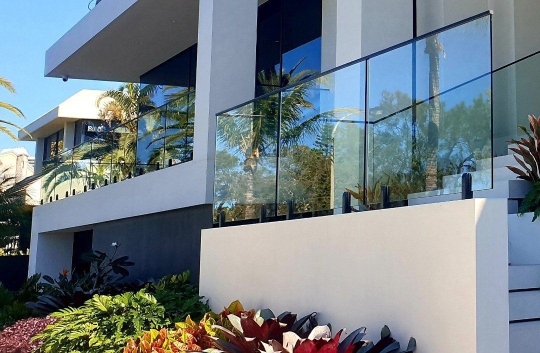 Modern white house with glass railing overlooking garden and greenery.