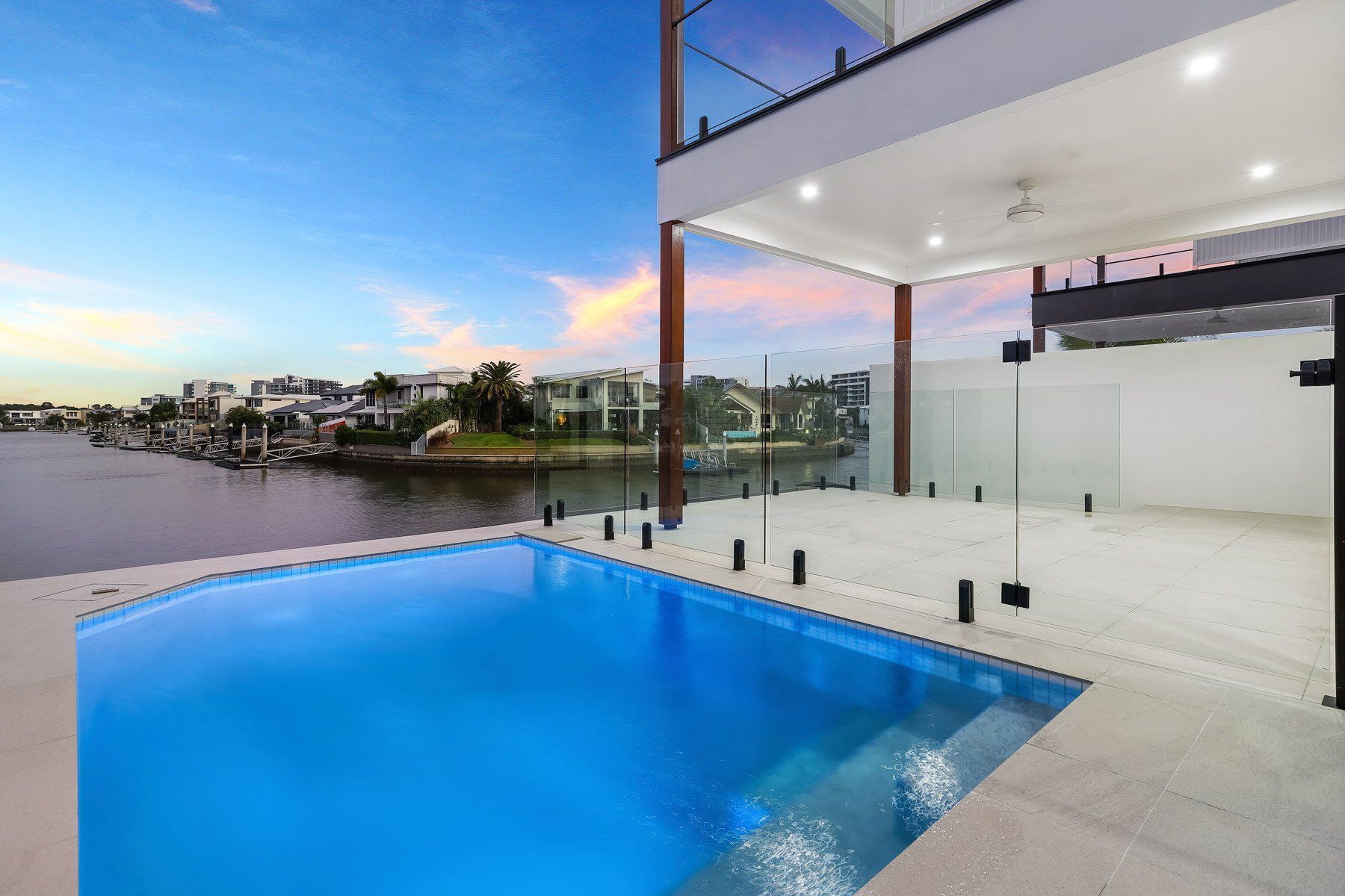 Swimming pool overlooking a waterway, modern house with glass railings.