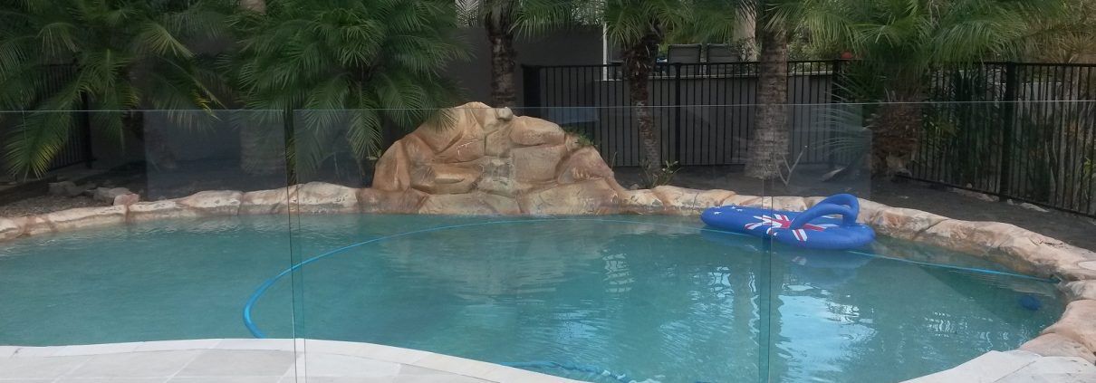 Swimming pool with a rock formation, blue floatie, and fence.