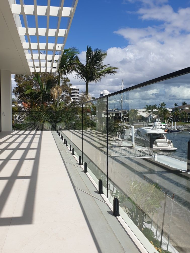 Balcony with glass railing overlooking a marina with white yachts and palm trees under a blue sky.