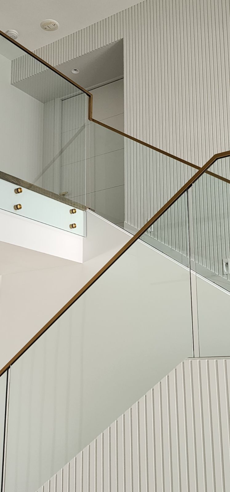 Modern staircase with glass railing and textured white wall.