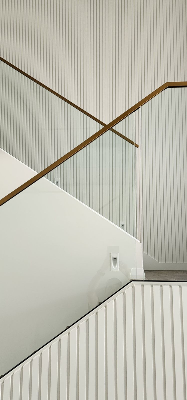 Staircase with white walls, wooden handrail, and textured walls in a minimalist design.