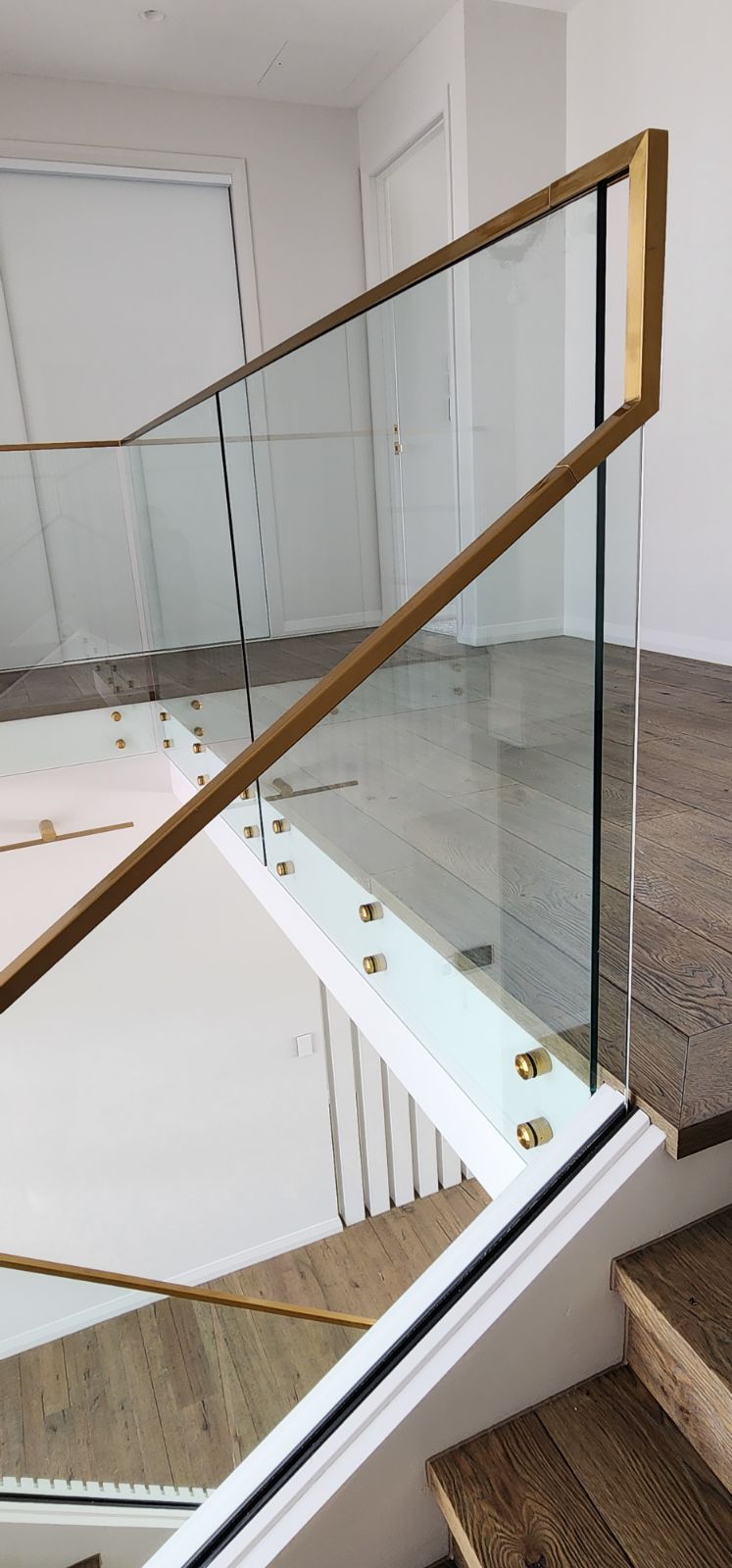 Staircase with glass railing and golden trim. Beige stairs and white wall.