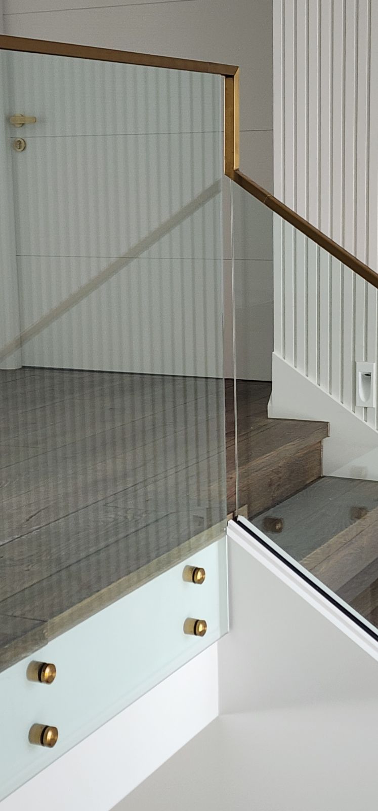 Staircase with glass railing and wooden handrail. White wall with vertical lines and wooden steps.