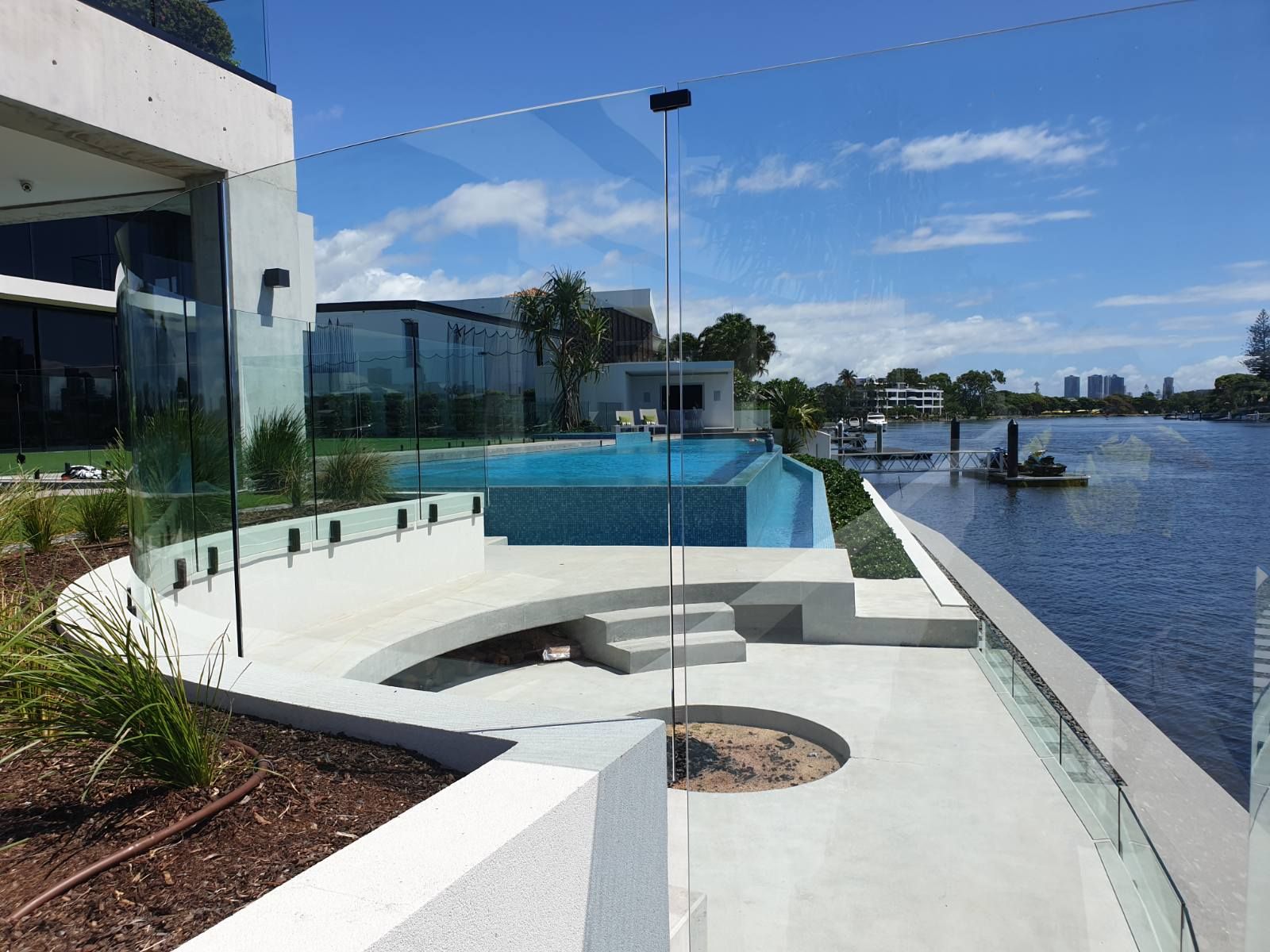 Modern waterfront home with a pool, clear glass fence, and canal view.