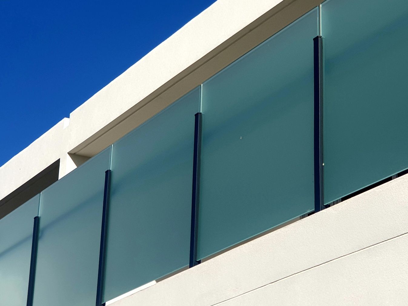 Frosted glass balcony with dark vertical supports against a clear blue sky.