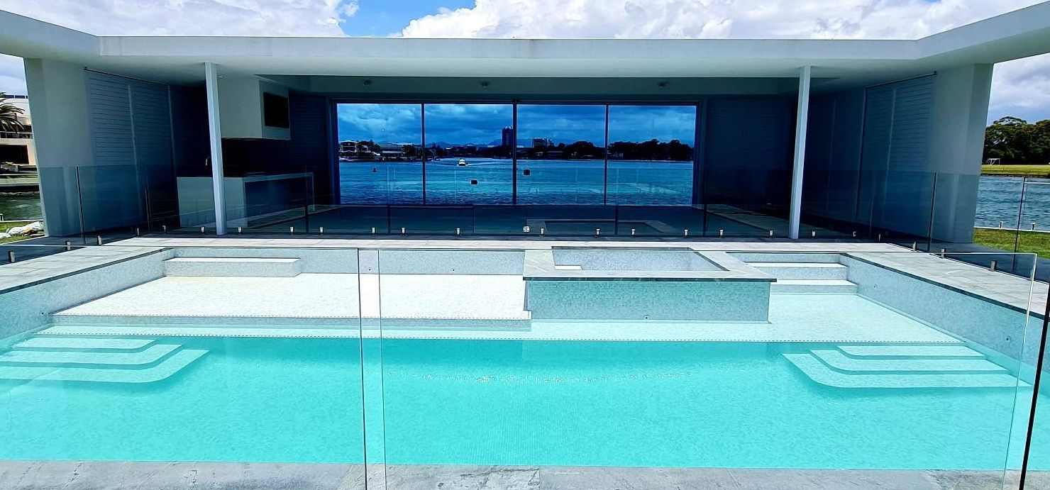 Modern building with pool. Large windows reflect a body of water. Turquoise pool with steps.