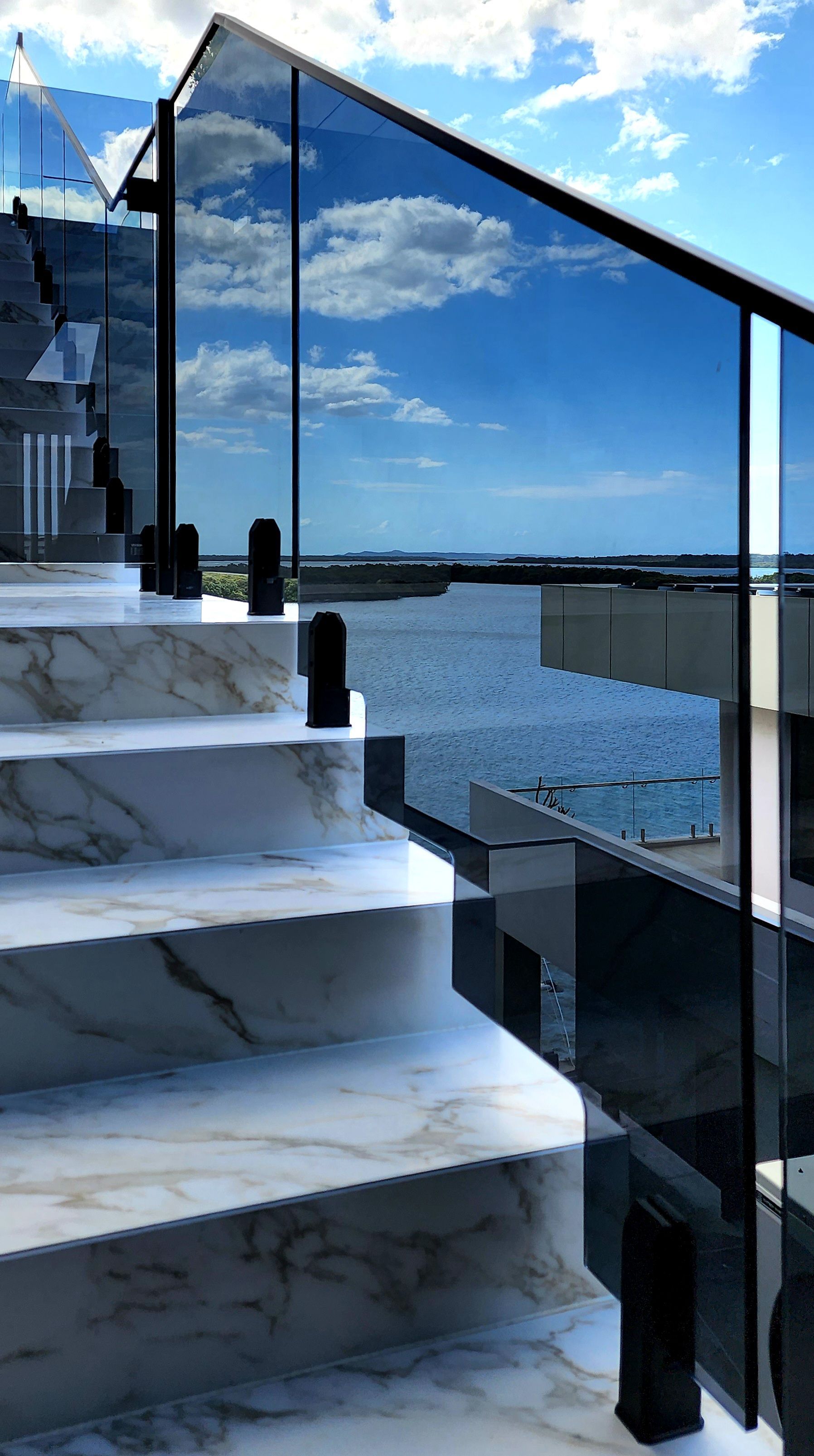 Marble staircase with glass railing reflecting sky and ocean view.