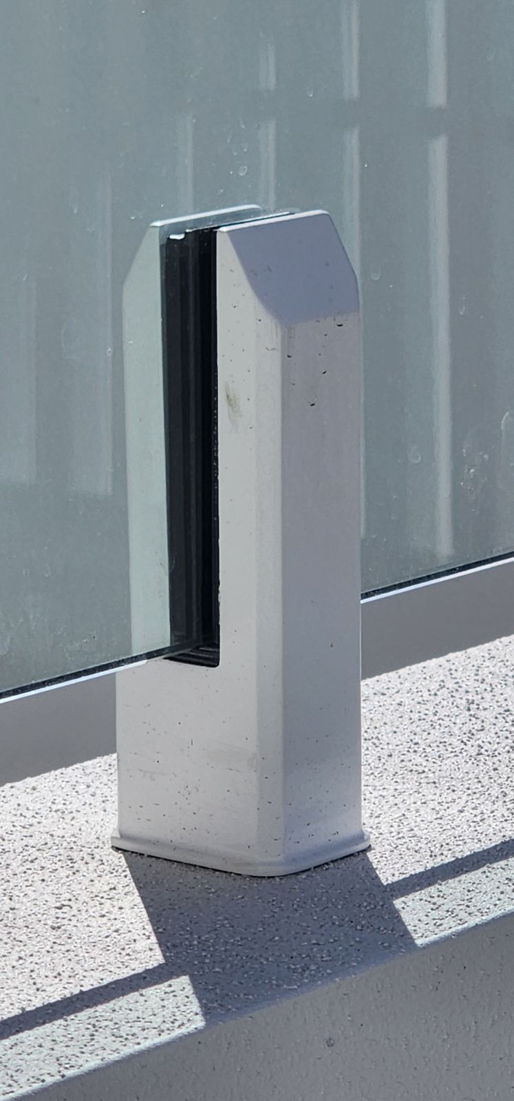 A white concrete pillar securing a glass panel, set on a light-colored surface.