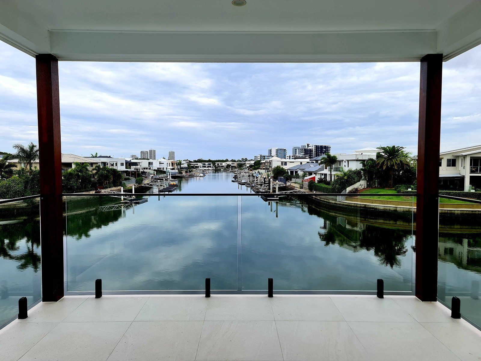 View of a canal lined with houses, seen from a balcony with glass railings and dark wood pillars.