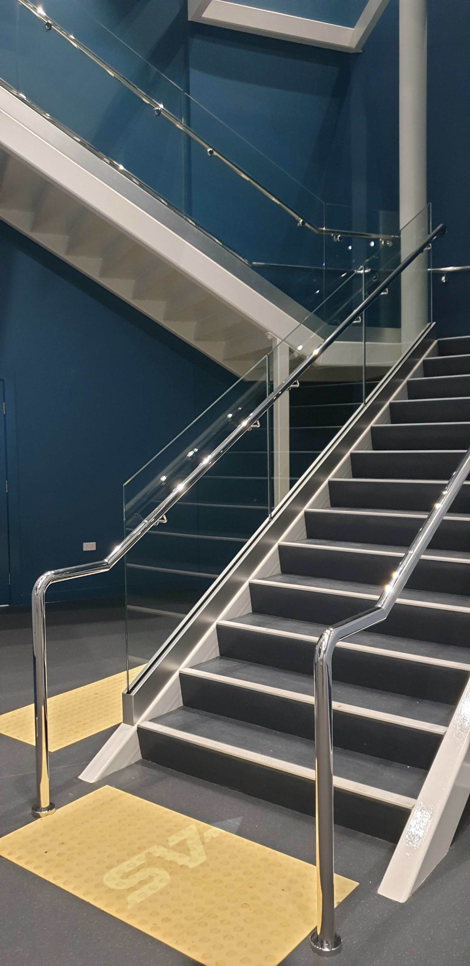 Staircase with dark gray steps, stainless steel railings, and navy blue walls.