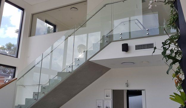 Modern staircase with glass railings, concrete steps, and white walls in a brightly lit interior.