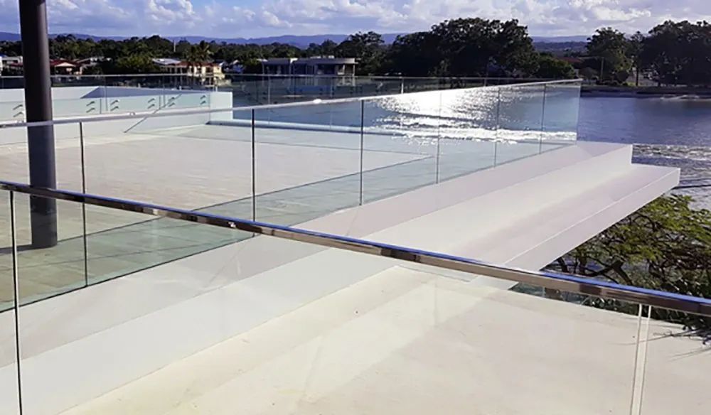 A modern waterfront patio with glass railings reflects the sun.