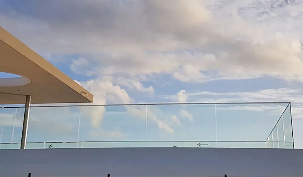 Modern rooftop with glass railing against a cloudy sky.