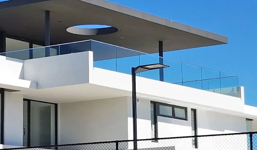 Modern white building with glass railings, a dark roof, and a clear blue sky.