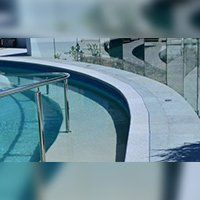 Curved pool with light blue water and a steel handrail, surrounded by a concrete deck.