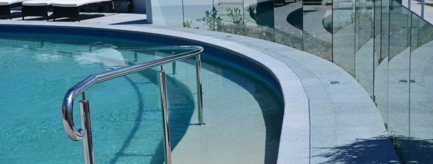 A curved swimming pool with a metal railing and a glass fence.