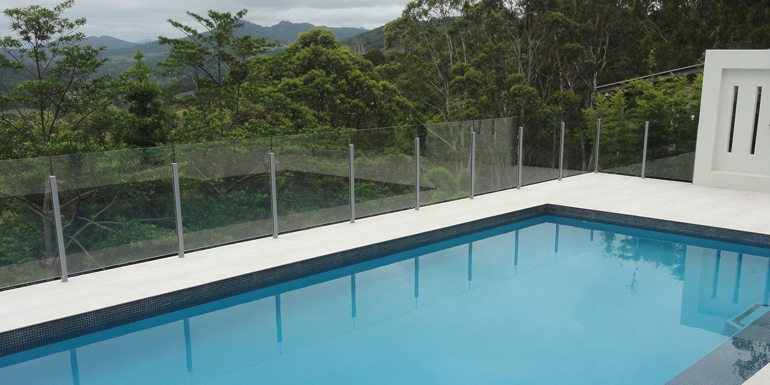 Poolside with glass fence, overlooking lush green hills.