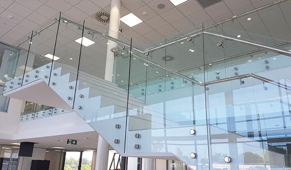 Glass staircase in a modern building with white steps and glass railings, under a bright ceiling.