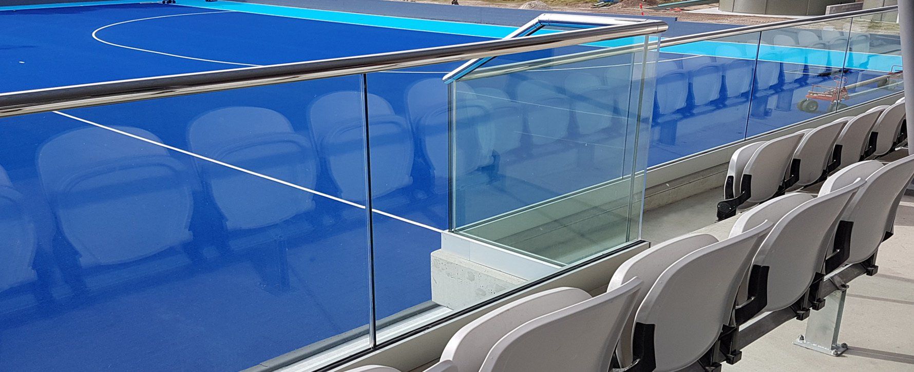 Empty stadium seating next to a blue hockey rink, separated by clear glass.