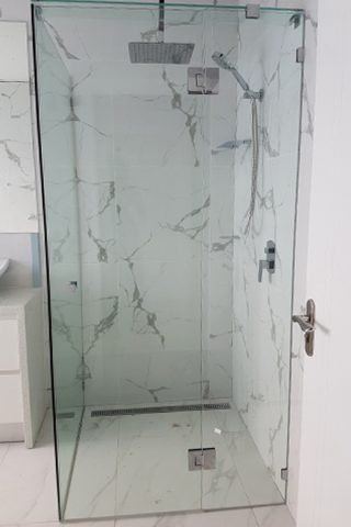 Glass shower enclosure with marble-look tile, chrome fixtures, and a handle on a white door.