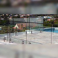 Glass railing around a pool area with a cityscape in the background.