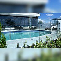 Pool area with glass fence and white building. Blue sky in the background.