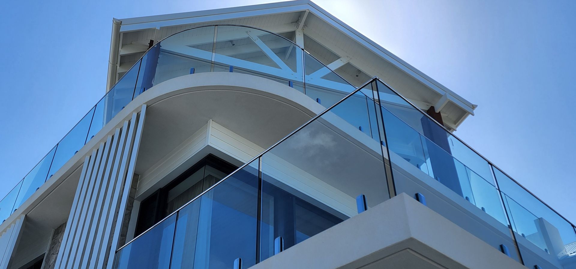 Modern building with glass balcony against a bright blue sky.