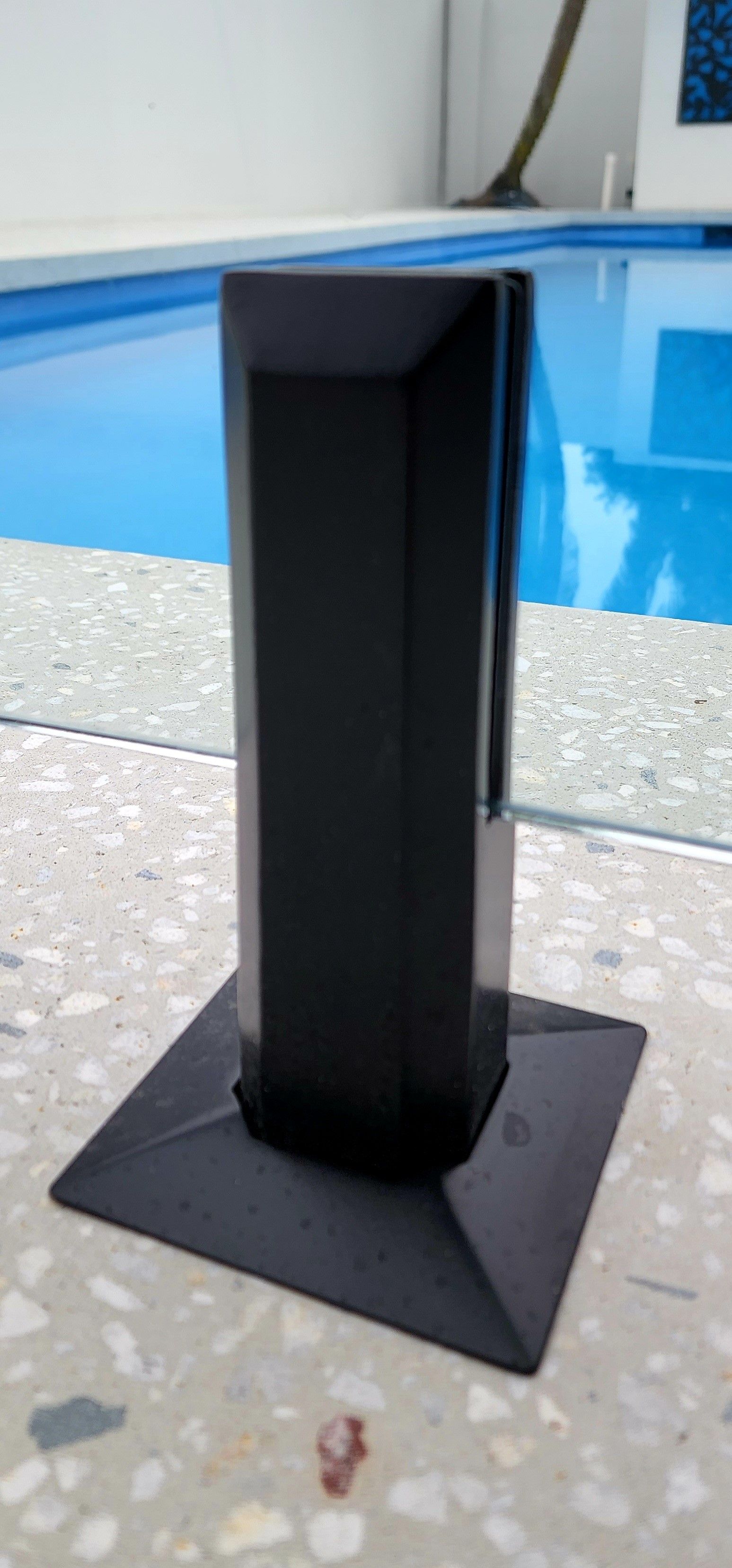 Black pillar with square base near a pool.