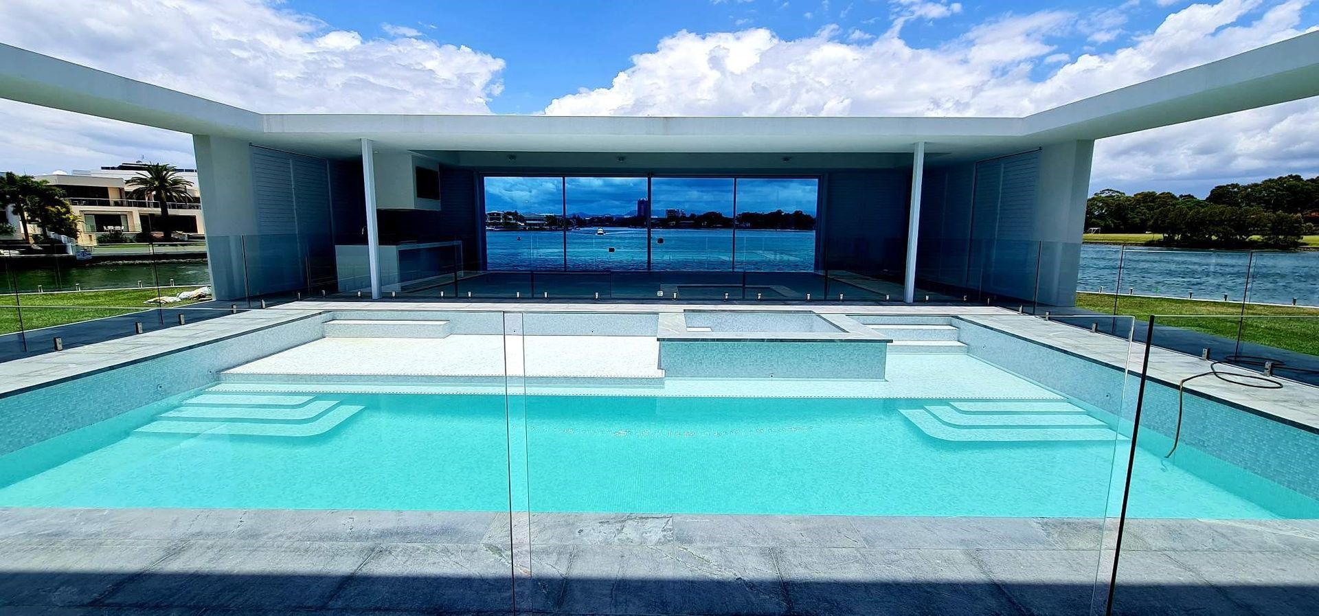 A modern house with a pool overlooking a lake. Blue sky, clear water, and white architecture.